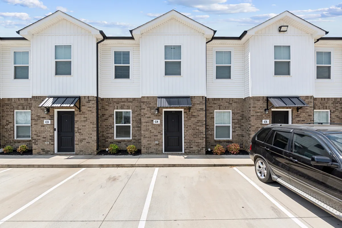 The exterior view showcases the welcoming front entrances of townhouse units, with well-maintained landscaping and a spacious parking area. The environment looks inviting, suggesting a peaceful and community-oriented setting ideal for families returning from local adventures.