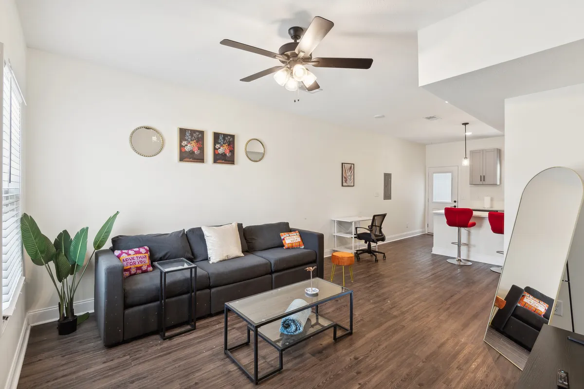 A warmly lit living room featuring a plush sofa, a stylish coffee table, tasteful artwork, and a large mirror that reflects the inviting atmosphere. The space looks designed for comfort and versatility, suitable for both relaxation and entertaining guests.