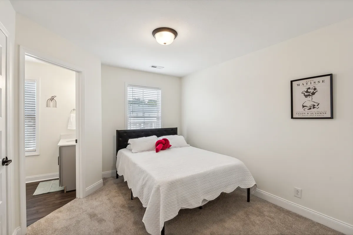 A cozy bedroom with a comfortable bed, framed artwork above the headboard, and a window that allows natural light to brighten the space. The setting conveys comfort, relaxation, and a sense of privacy.