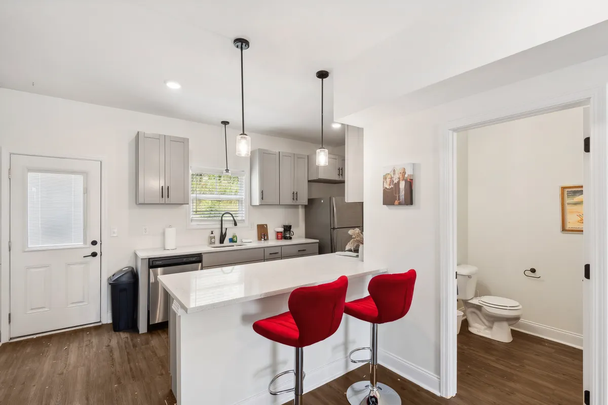A stylish kitchen scene with vivid red bar stools framing a spacious island, surrounded by sleek modern cabinetry and open sightlines to the rest of the living area. The kitchen exudes a warm, welcoming atmosphere perfect for casual dining or entertaining friends and family. The design emphasizes the open layout and social possibilities.